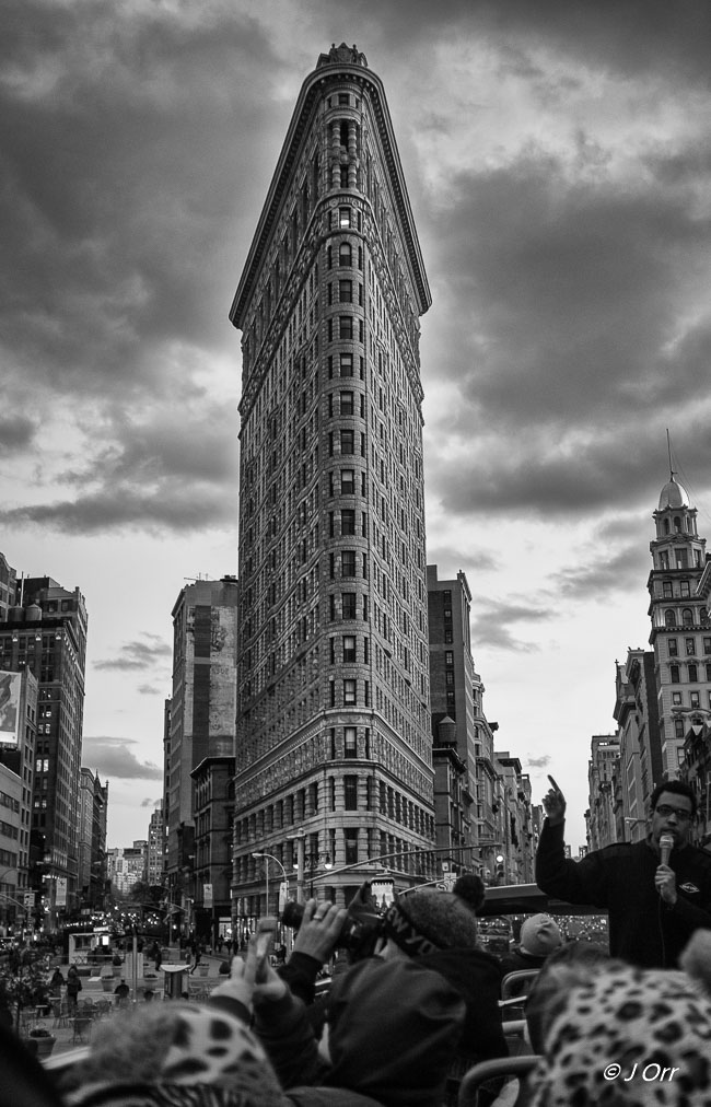 New York Bus Tour with the Flatiron Building. The Flatiron Building, originally the Fuller Building, was completed in 1902. It sits on a triangular block formed by Fifth Avenue, Broadway, and East 22nd Street